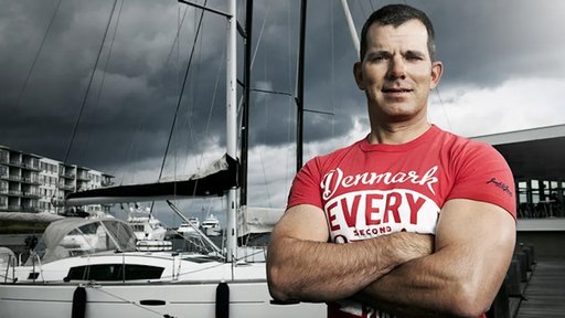 Claus Olesen i t-shirt med korslagte arme foran både i havnen
